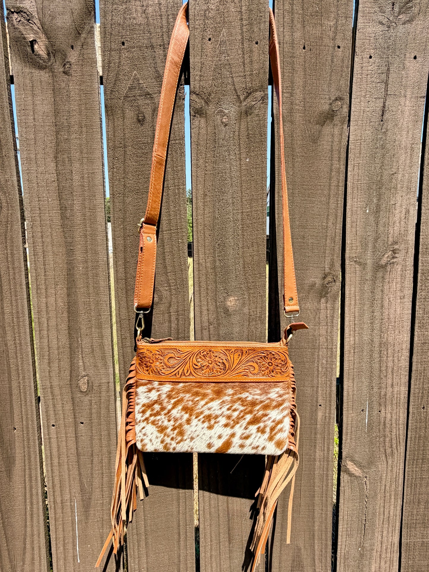 Handcrafted genuine cowhide crossbody bag with floral tooled leather, long leather fringe, adjustable strap, and zip-top closure for western, rodeo, and everyday style.
