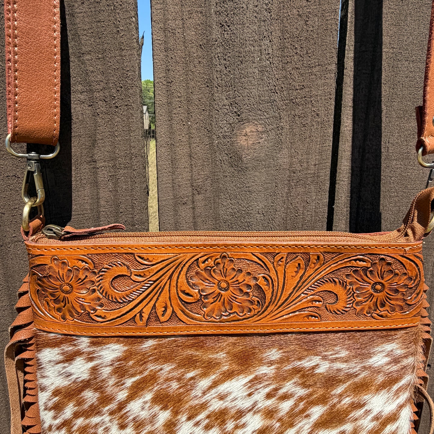Handcrafted genuine cowhide crossbody bag with floral tooled leather, long leather fringe, adjustable strap, and zip-top closure for western, rodeo, and everyday style.