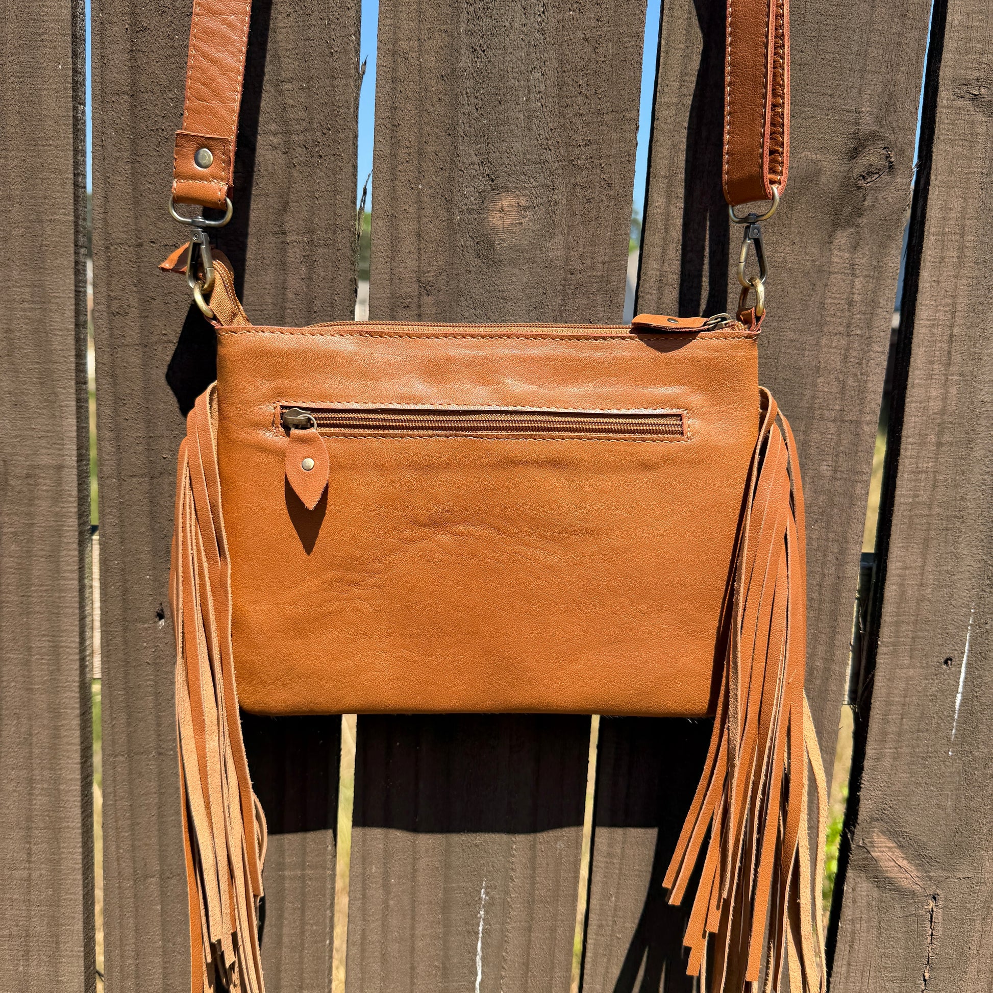 Handcrafted genuine cowhide crossbody bag with floral tooled leather, long leather fringe, adjustable strap, and zip-top closure for western, rodeo, and everyday style.