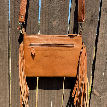 Handcrafted genuine cowhide crossbody bag with floral tooled leather, long leather fringe, adjustable strap, and zip-top closure for western, rodeo, and everyday style.