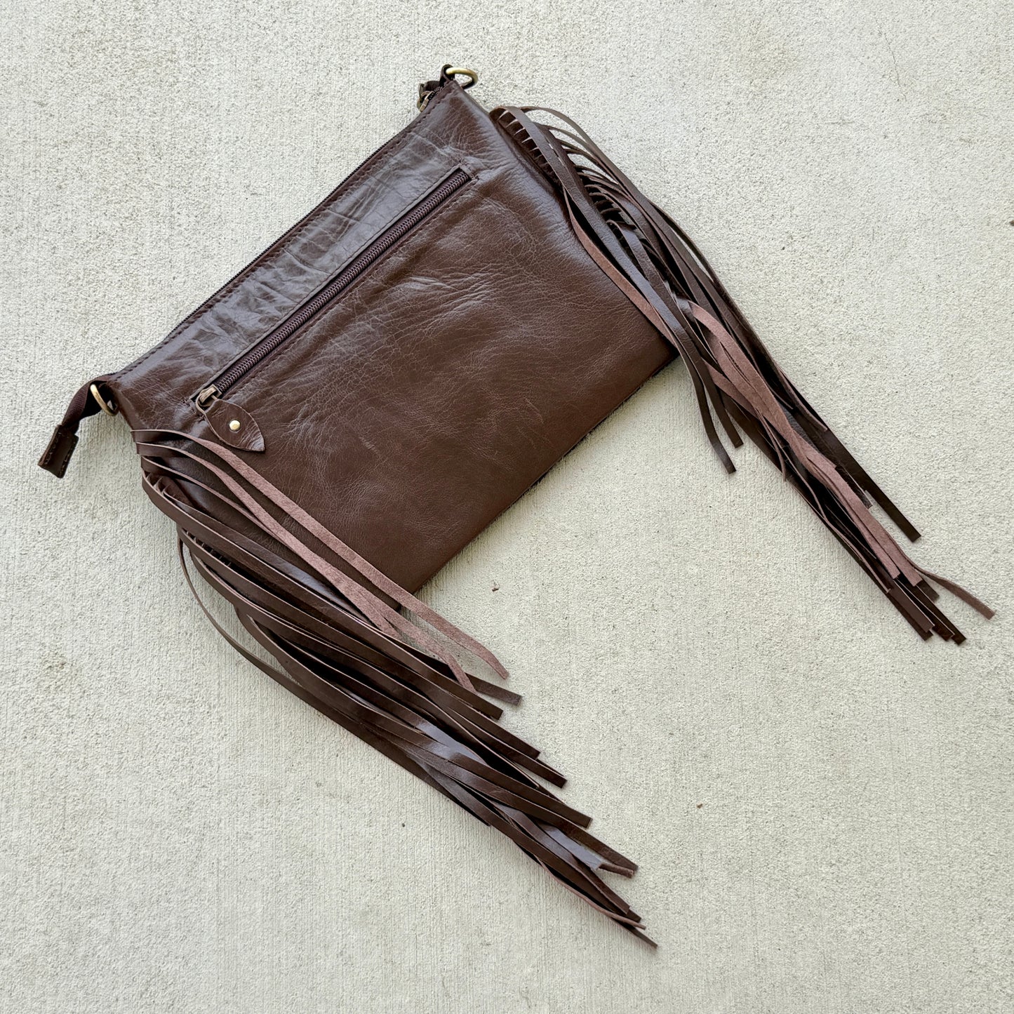 Handcrafted genuine cowhide crossbody bag with floral tooled leather, long leather fringe, adjustable strap, and zip-top closure for western, rodeo, and everyday style.