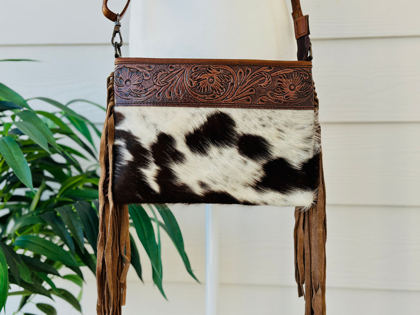 Handcrafted genuine cowhide crossbody bag with floral tooled leather, long leather fringe, adjustable strap, and zip-top closure for western, rodeo, and everyday style.