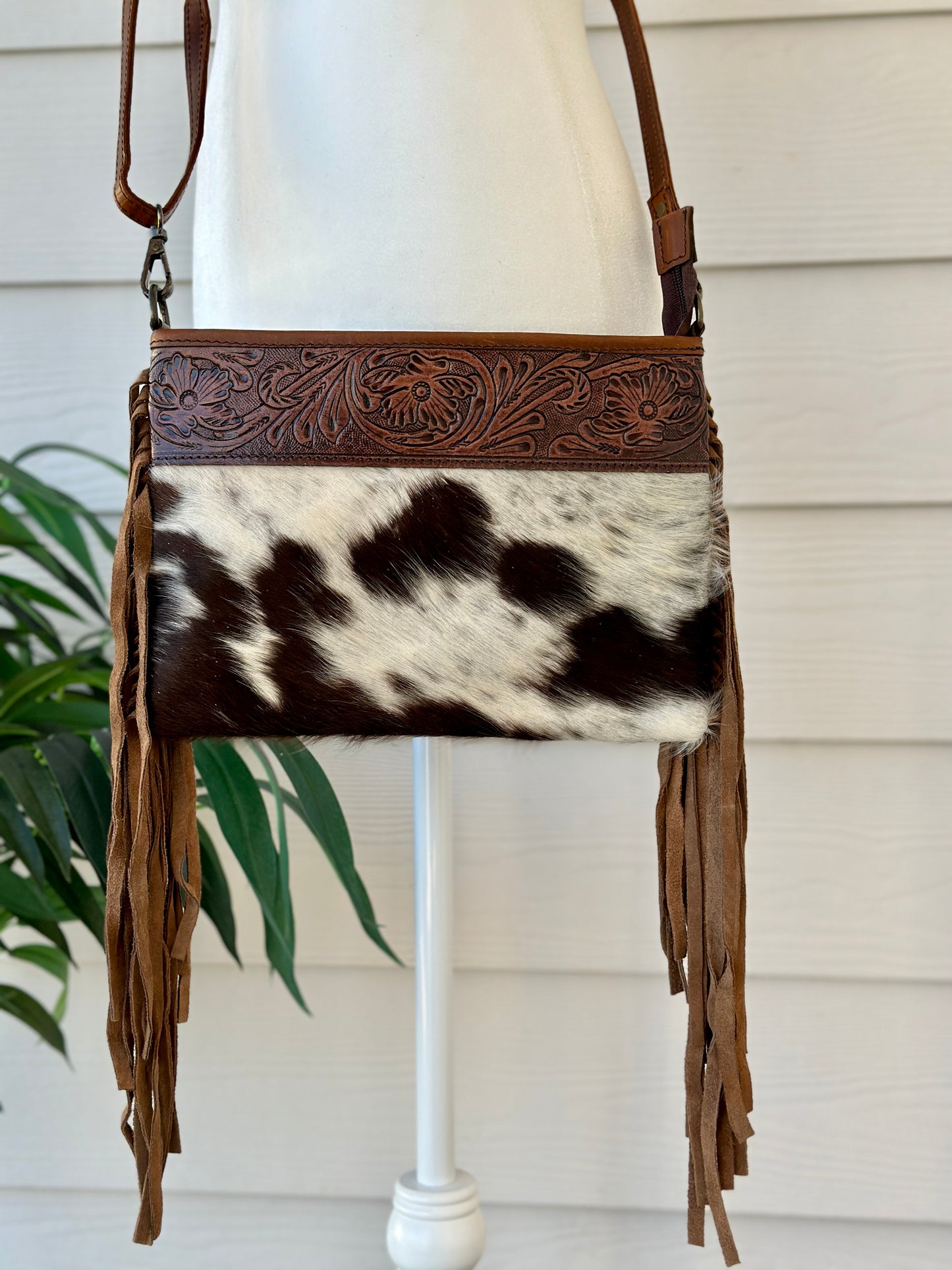 Handcrafted genuine cowhide crossbody bag with floral tooled leather, long leather fringe, adjustable strap, and zip-top closure for western, rodeo, and everyday style.