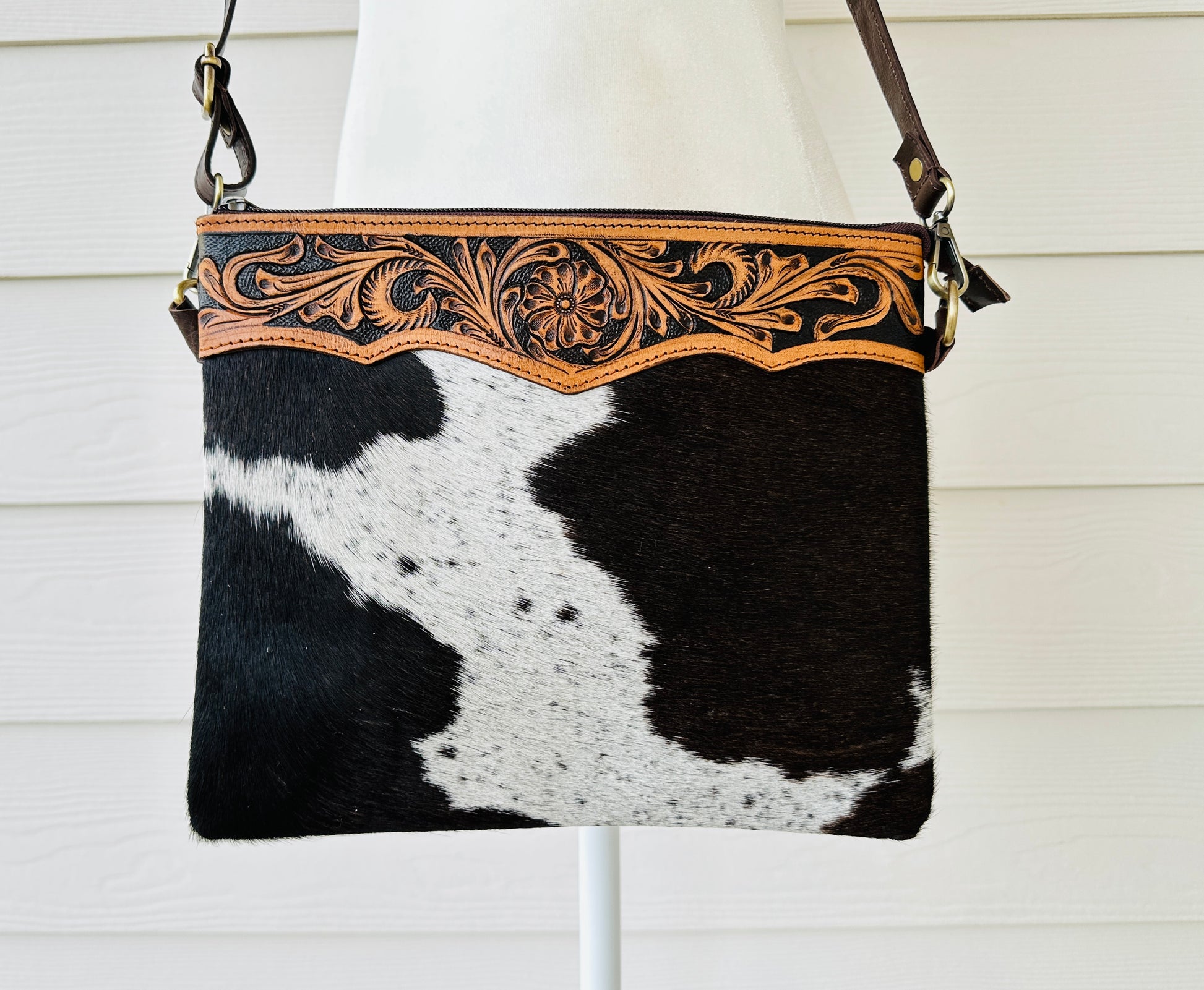 Handcrafted genuine cowhide crossbody purse with floral tooled leather zipper accent, adjustable leather strap, and western hair-on-hide design for everyday wear and rodeos.