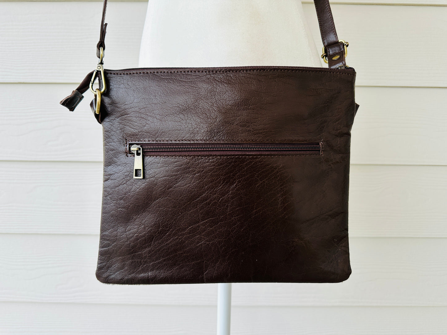 Handcrafted genuine cowhide crossbody purse with floral tooled leather zipper accent, adjustable leather strap, and western hair-on-hide design for everyday wear and rodeos.