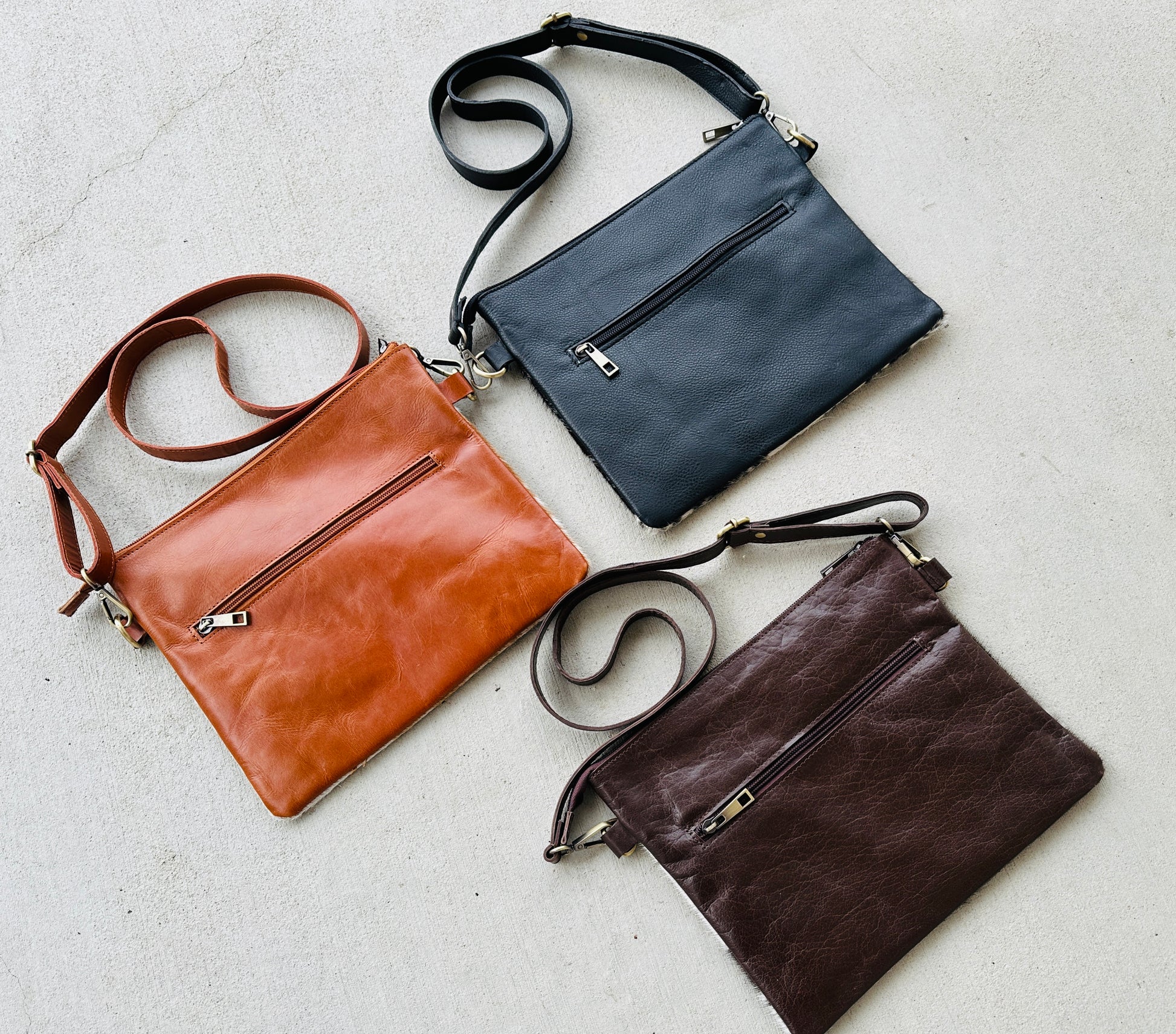 Handcrafted genuine cowhide crossbody purse with floral tooled leather zipper accent, adjustable leather strap, and western hair-on-hide design for everyday wear and rodeos.