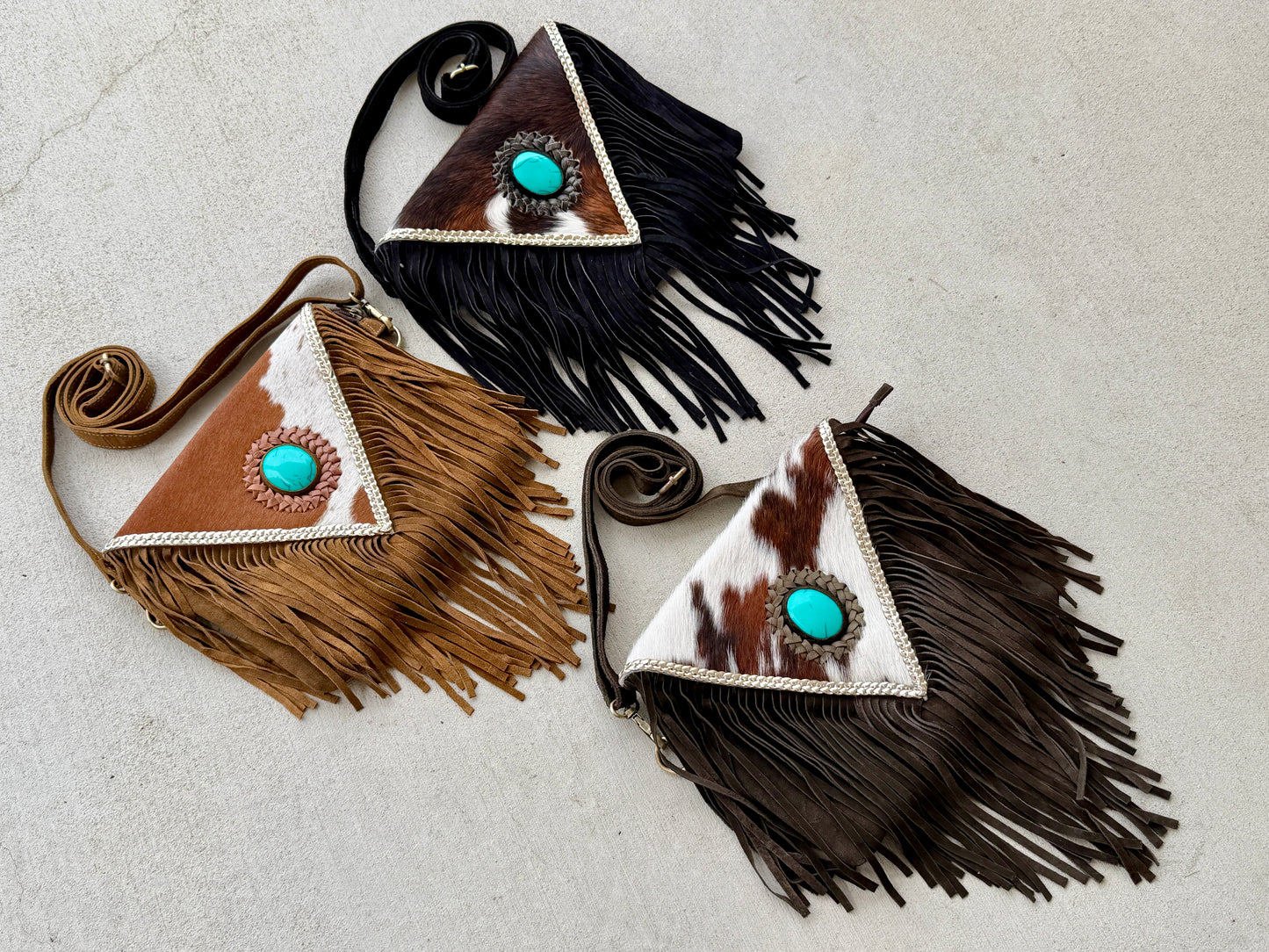 Handcrafted western cowhide crossbody bag with turquoise stone concho, whipstitched envelope flap, long leather fringe, and adjustable strap for rodeos, concerts, and everyday wear.