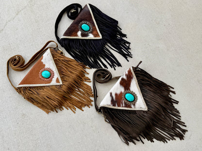 Handcrafted western cowhide crossbody bag with turquoise stone concho, whipstitched envelope flap, long leather fringe, and adjustable strap for rodeos, concerts, and everyday wear.