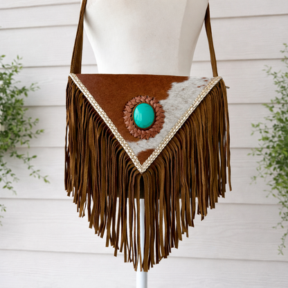 Handcrafted western cowhide crossbody bag with turquoise stone concho, whipstitched envelope flap, long leather fringe, and adjustable strap for rodeos, concerts, and everyday wear.