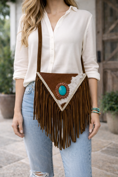 Handcrafted western cowhide crossbody bag with turquoise stone concho, whipstitched envelope flap, long leather fringe, and adjustable strap for rodeos, concerts, and everyday wear.